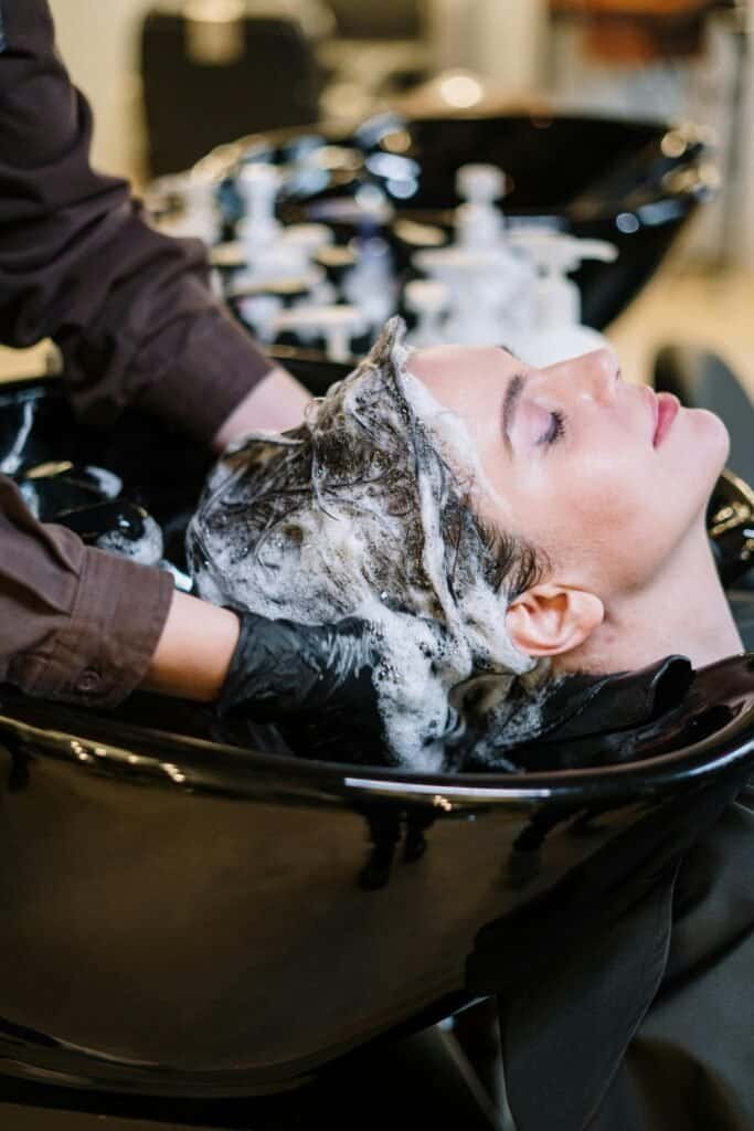 Professional scalp cleansing at hair salon showing proper shampooing technique with focus on scalp massage and thorough lather
