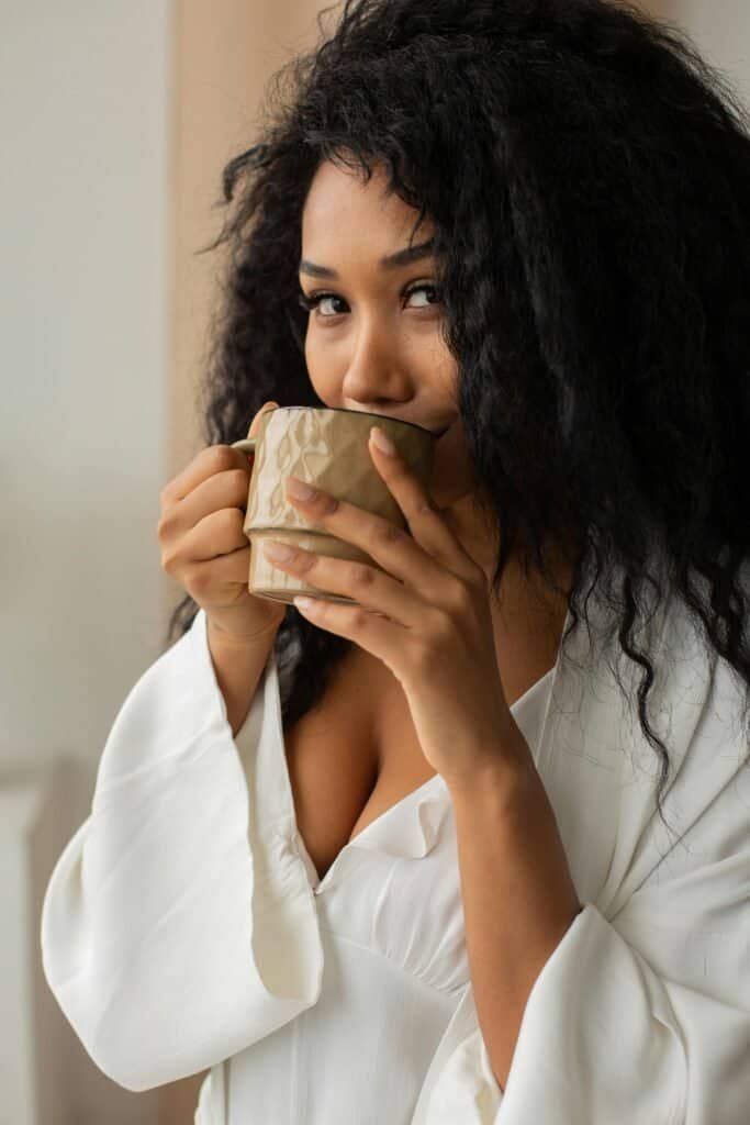 Woman with textured hair enjoying morning self-care routine emphasizing importance of consistent hair washing schedule for scalp health