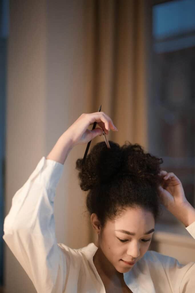 Black woman with natural coily hair styling into bun demonstrating balance between protective styling and scalp health maintenance