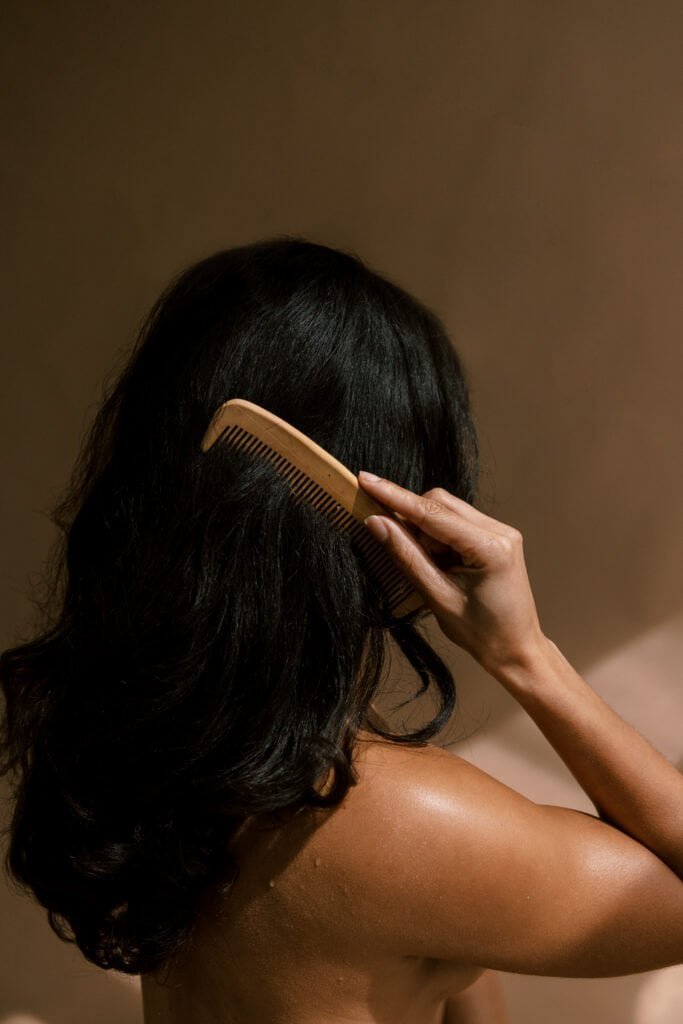 Woman combing healthy dark hair with wooden comb, showing results of proper scalp care routine