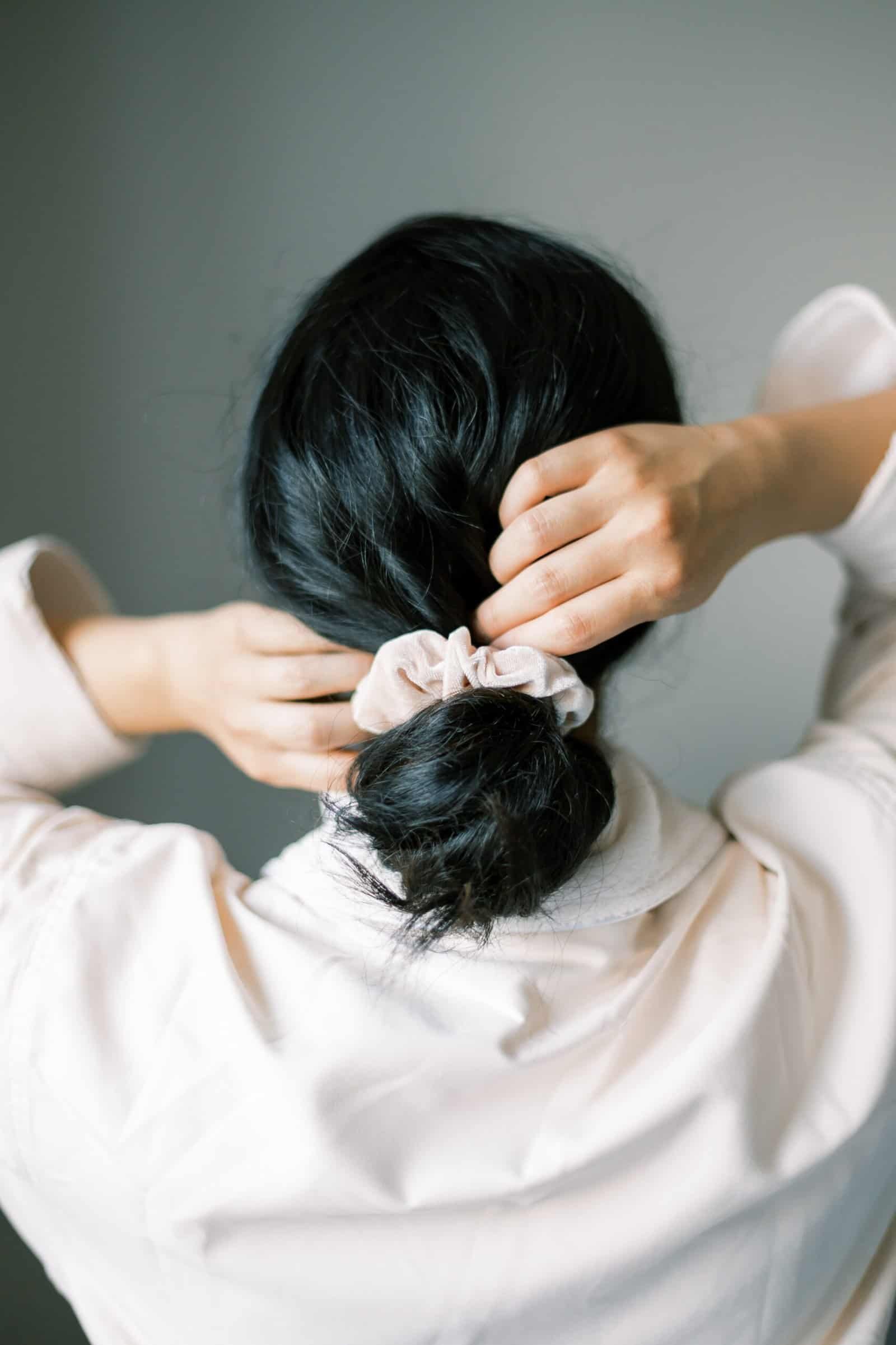 Healthy dark hair being styled into ponytail, showcasing strong shiny hair from proper scalp care