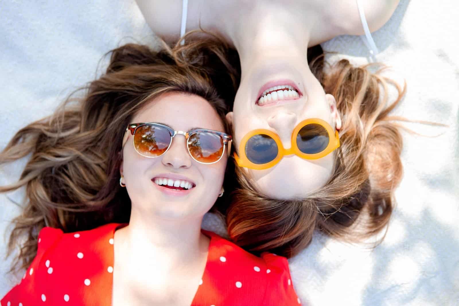Two happy women displaying healthy, shiny hair from good scalp care, lying together and smiling