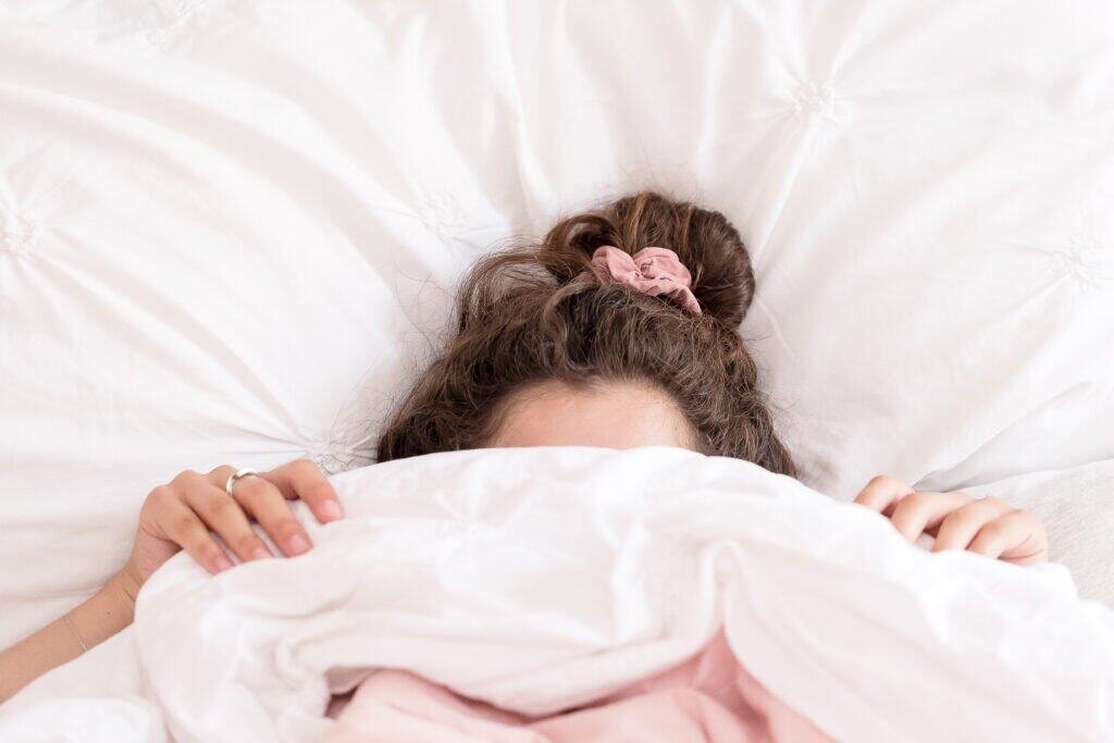 Woman with healthy hair in messy bun resting in bed, showing importance of sleep for scalp health