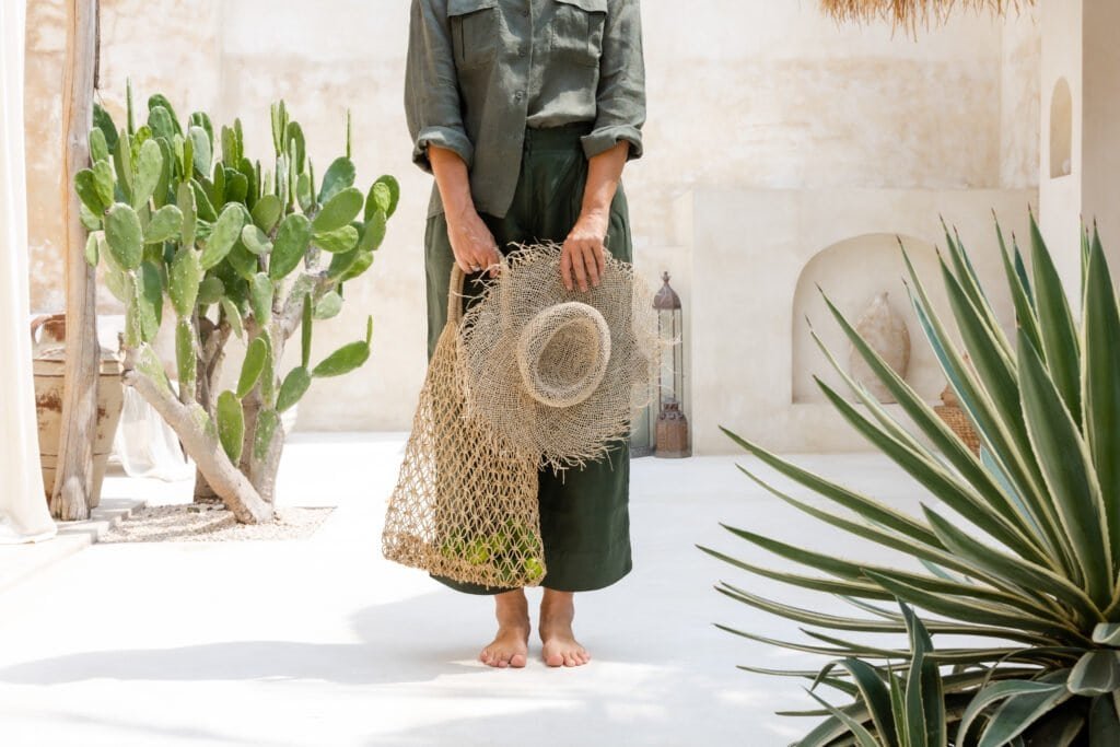 Woman wearing long-sleeved protective clothing and holding a wide-brimmed hat in a woven bag, demonstrating essential sun protection accessories for preventing hydroquinone-induced hyperpigmentation during treatment.