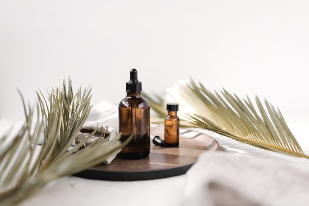 DIY natural sunburn treatment serum in amber glass dropper bottles with dried palm fronds. The tinted bottles protect the healing oils while the minimal aesthetic highlights the natural botanical ingredients used in homemade remedies for sun-damaged skin