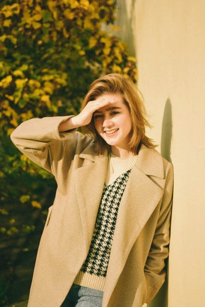 Smiling fair-skinned young woman shielding her eyes from sunlight against an autumn background, representing high photosensitivity skin types that benefit most from natural photoprotective supplements like silymarin and niacinamide