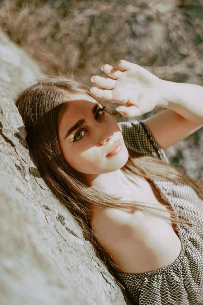 Young woman shielding sun-exposed skin from intense UV rays with her hand, representing the need for effective natural sunburn treatment and photoprotection using plant-based remedies
