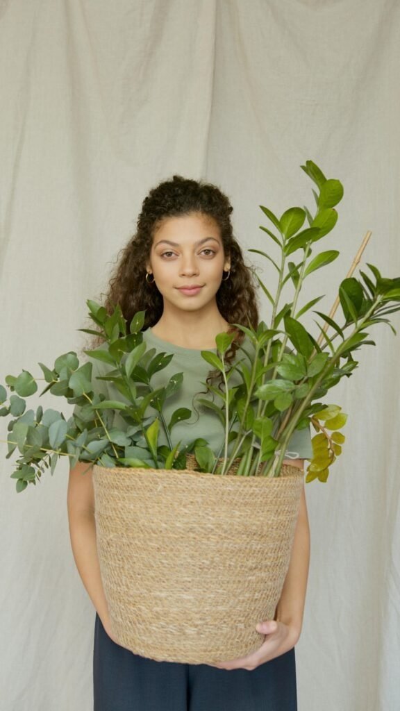 Young woman with curly hair holding a large basket of lush green plants, representing the botanical origin of silymarin from milk thistle and its natural photoprotective antioxidant properties for skin cancer prevention