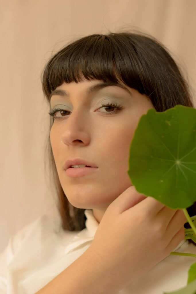 Woman with natural skin holding a round Centella Asiatica leaf near her face, representing the ancient healing herb's role in natural sunburn treatment by accelerating tissue repair and rebuilding collagen