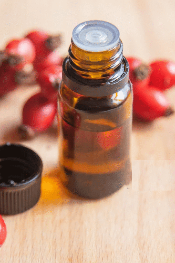 Amber glass bottle of rosehip oil beside fresh red rosehips on a wooden surface, showcasing the CO2-extracted oil used for natural sunburn treatment, collagen repair, and photoaging prevention
