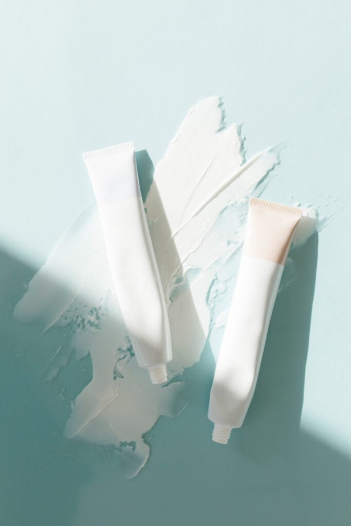 Two white skincare cream tubes with product smears on a blue background, representing mineral sunscreen options like zinc oxide and titanium dioxide recommended for personalized photosensitivity-based sun protection