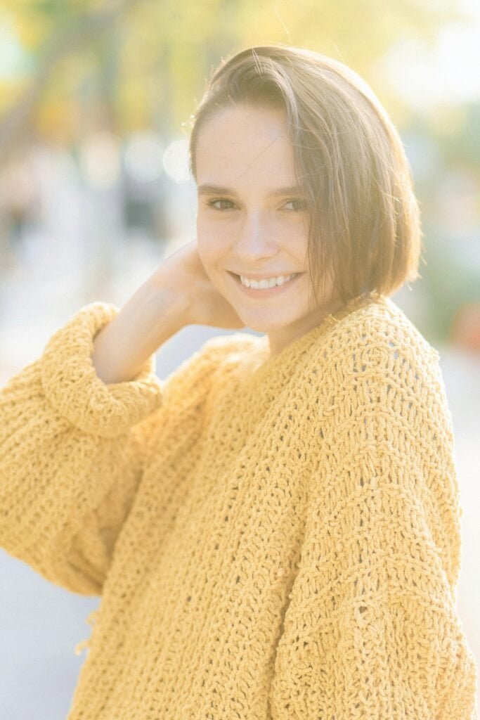 miling fair-skinned woman with blonde bob in warm sunlight wearing a yellow sweater, representing Fitzpatrick skin type III with moderate photosensitivity and an adaptive tanning response to UV exposure