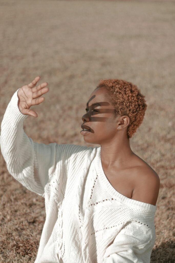 Black woman with short natural hair shielding her face from sunlight with her raised hand, illustrating how niacinamide complements melanin's UV protection to prevent hyperpigmentation in Black skin
