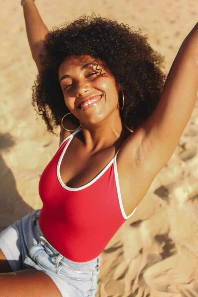 Joyful Black woman with natural curly hair at the beach under direct sunlight, reflecting the significantly lower skin cancer risk in melanin-rich skin and the safety of outdoor sun enjoyment