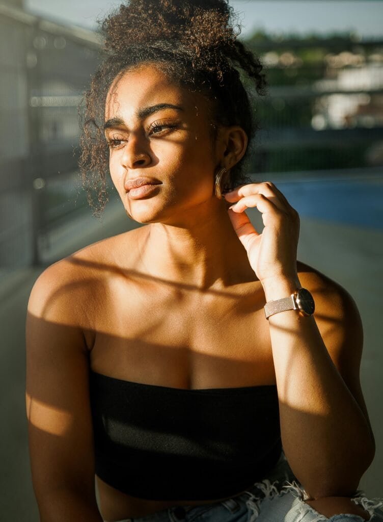 Close-up portrait of a Black woman's melanin-rich skin illuminated by dramatic direct sunlight, visually illustrating how melanin acts as a natural shield against UV-induced DNA damage and skin cancer