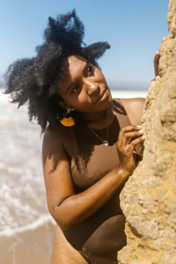 Dark-skinned Black woman with natural afro hair smiling at the beach, representing the enhanced photoprotection achieved by combining melanin's natural defenses with Polypodium leucotomos supplements