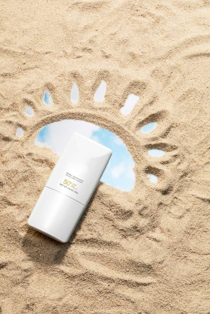 SPF 50 sunscreen bottle resting on beach sand with a sun drawing, illustrating how sunscreen works as UV protection while highlighting the limitations of high SPF ratings discussed in the truth about sunscreen