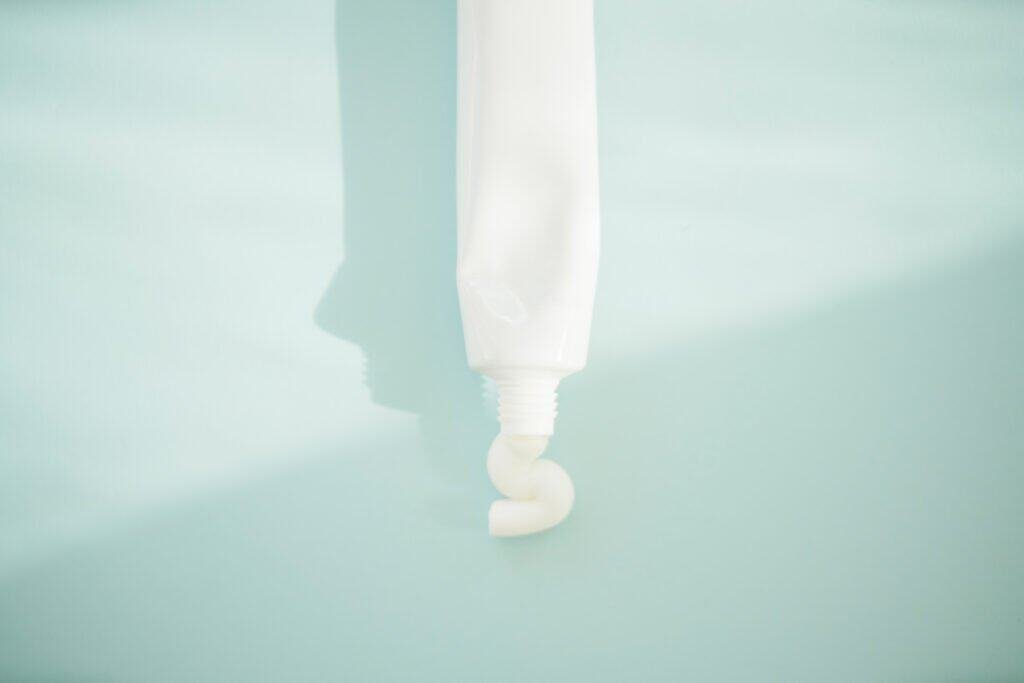 Close-up of white sunscreen being squeezed from a tube against a light blue background, illustrating chemical ingredients discussed in 'The Truth About Sunscreen: 8 Facts The Industry Doesn't Want You To Know' about what's actually in your sunscreen products