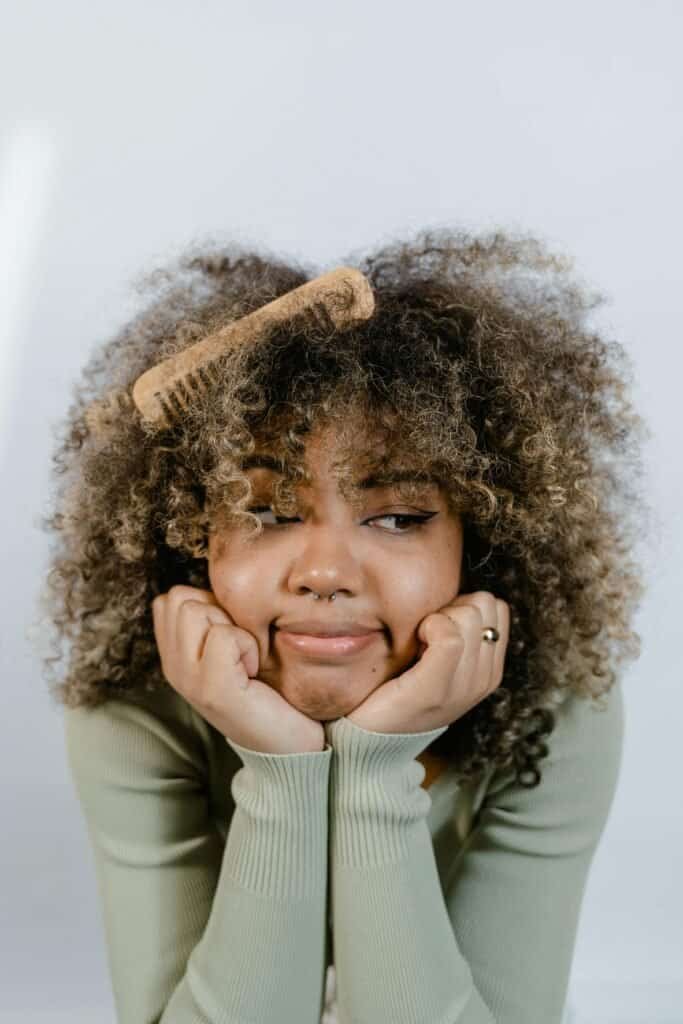 African woman with vibrant healthy curly Afro hair using wooden comb illustrating successful moisture-focused care and weekly washing routine benefits