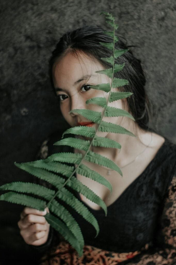 Woman peering through fresh Polypodium fern leaves representing the connection between natural botanicals and skin protection