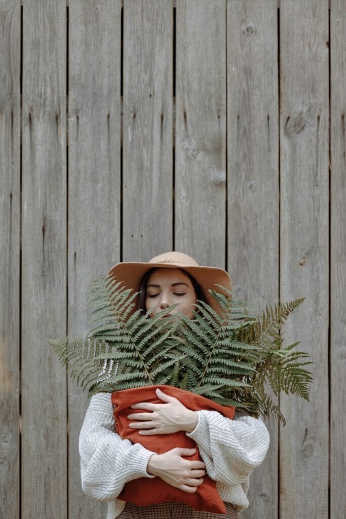 Woman in sun hat holding fresh fern fronds representing natural botanical sun protection and skincare