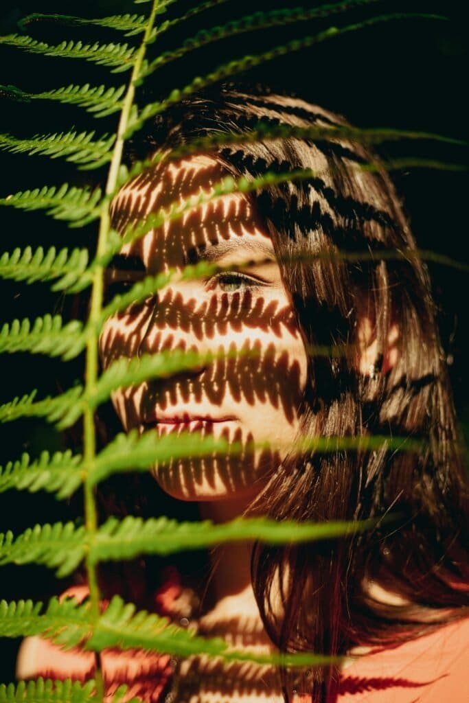 Woman with fern leaf shadow pattern on face symbolizing natural sun protection and UV defense from Polypodium leucotomos