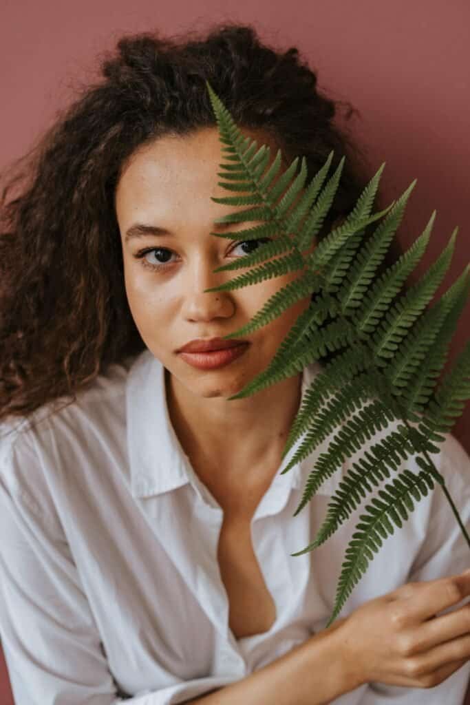 Portrait of woman with fern leaf covering half her face showcasing natural beauty and plant-based skin protection