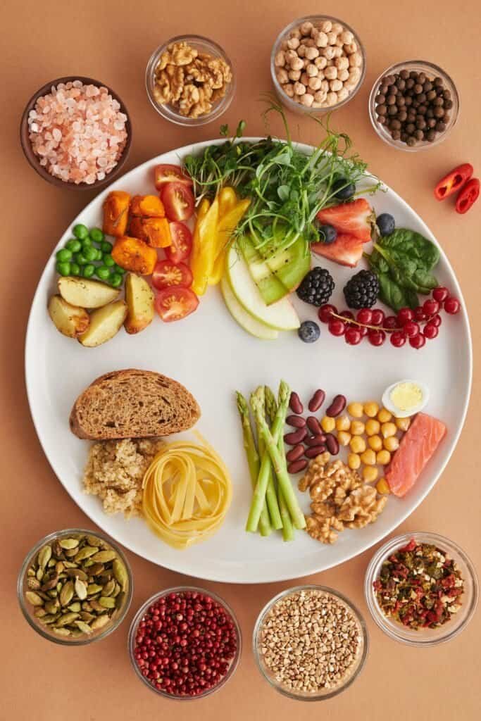 White plate surrounded by bowls of anti-acne whole foods including salmon, legumes, berries, vegetables, nuts, and whole grains representing a balanced low-GL diet for acne-prone skin