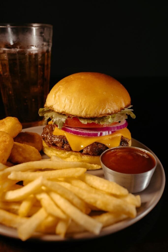 Cheeseburger with french fries and cola on a dark background representing high glycemic load Western diet foods that trigger acne breakouts through insulin and IGF-1 signaling