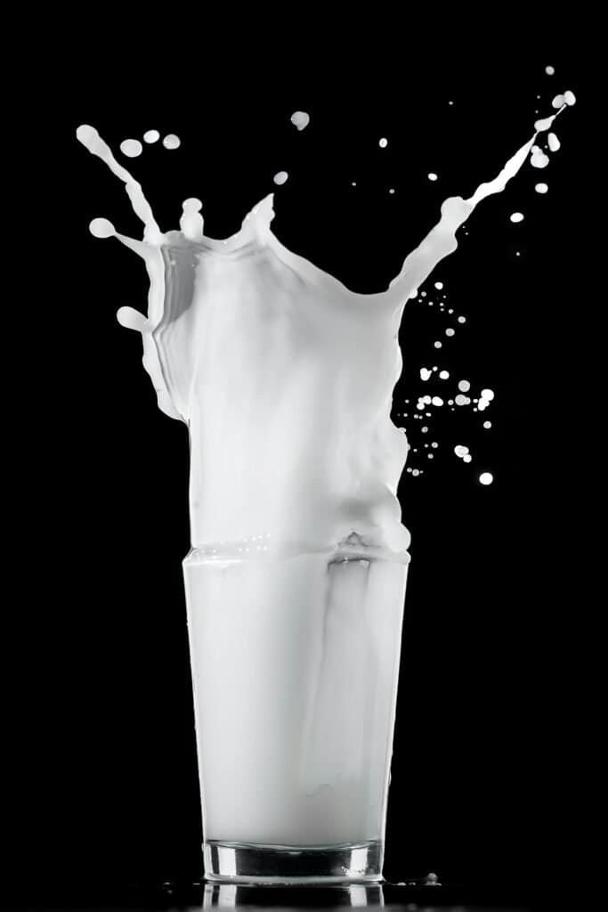 Dramatic milk splash in a glass on a black background illustrating the link between dairy consumption and increased acne risk and severity through hormonal and protein pathways