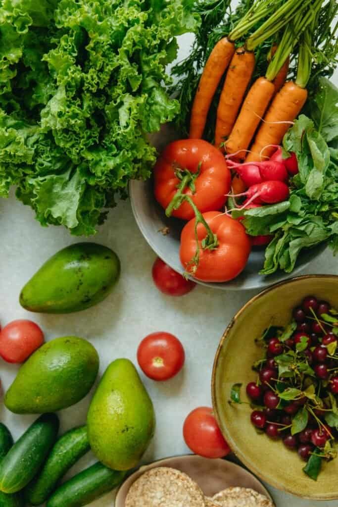 Flat lay of fresh whole foods including tomatoes, carrots, avocados, and cherries representing a low glycemic anti-acne diet for clearer skin