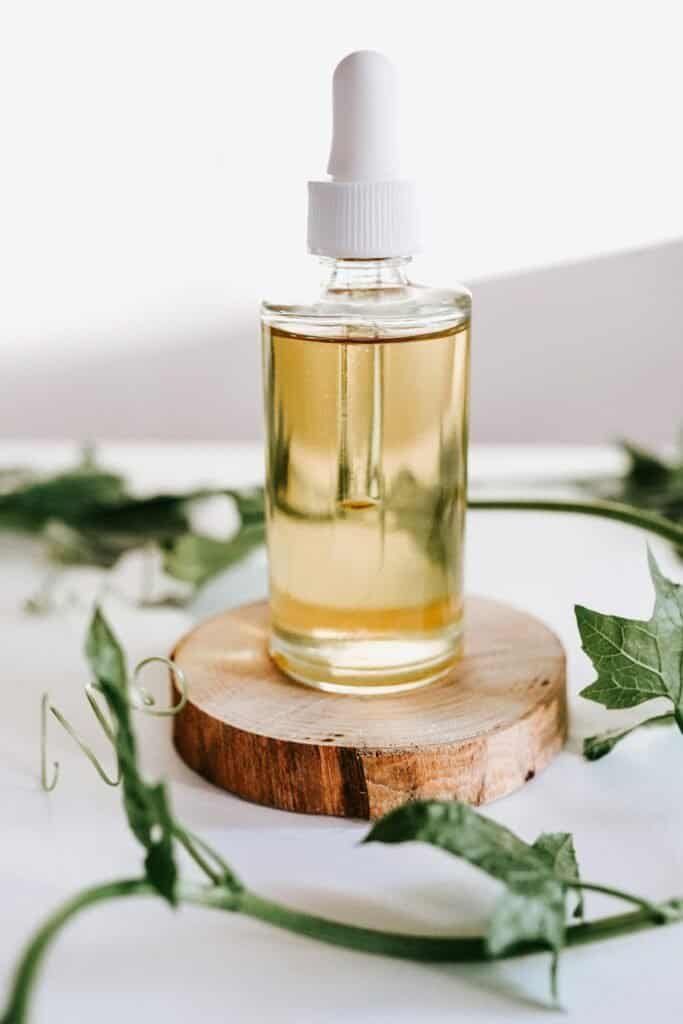 Glass dropper bottle containing a natural botanical serum on a wood slice surrounded by green ivy leaves, representing science-backed plant-based skincare for acne-prone skin